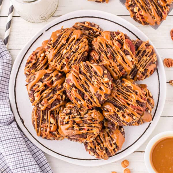 Square image of Easy Turtle Cookies piled on a serving plate with caramel drizzle and chopped pecans.