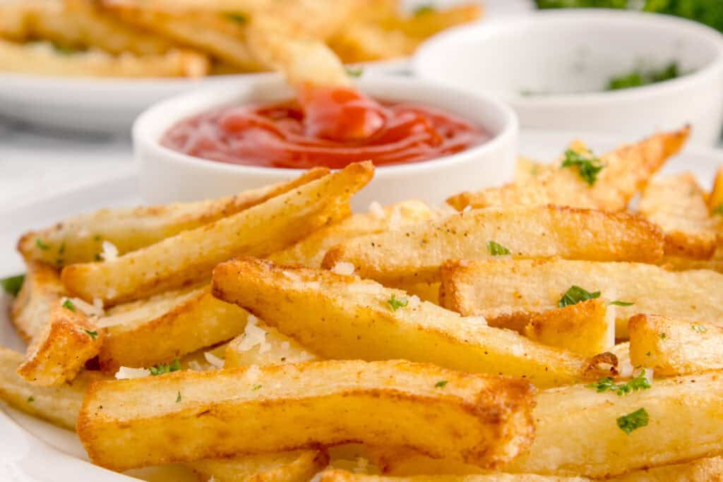 Close-up of golden Air Fryer French Fries topped with Parmesan and parsley beside ketchup