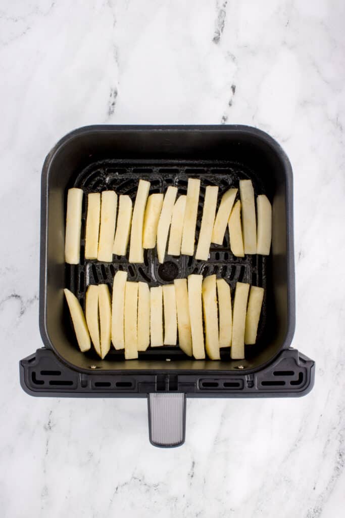 Uncooked French fries arranged in a single layer in an air fryer basket
