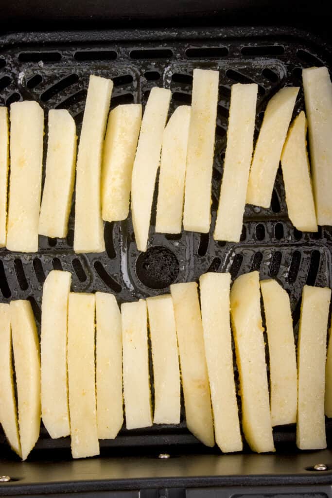 Close-up of seasoned potato fries arranged in a single layer in an air fryer basket