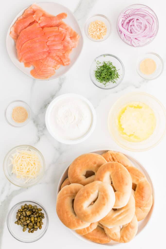 Ingredients for Baked Bagels & Lox Sliders including mini bagels, smoked salmon, cream cheese, red onion, capers, dill, butter, and Parmesan