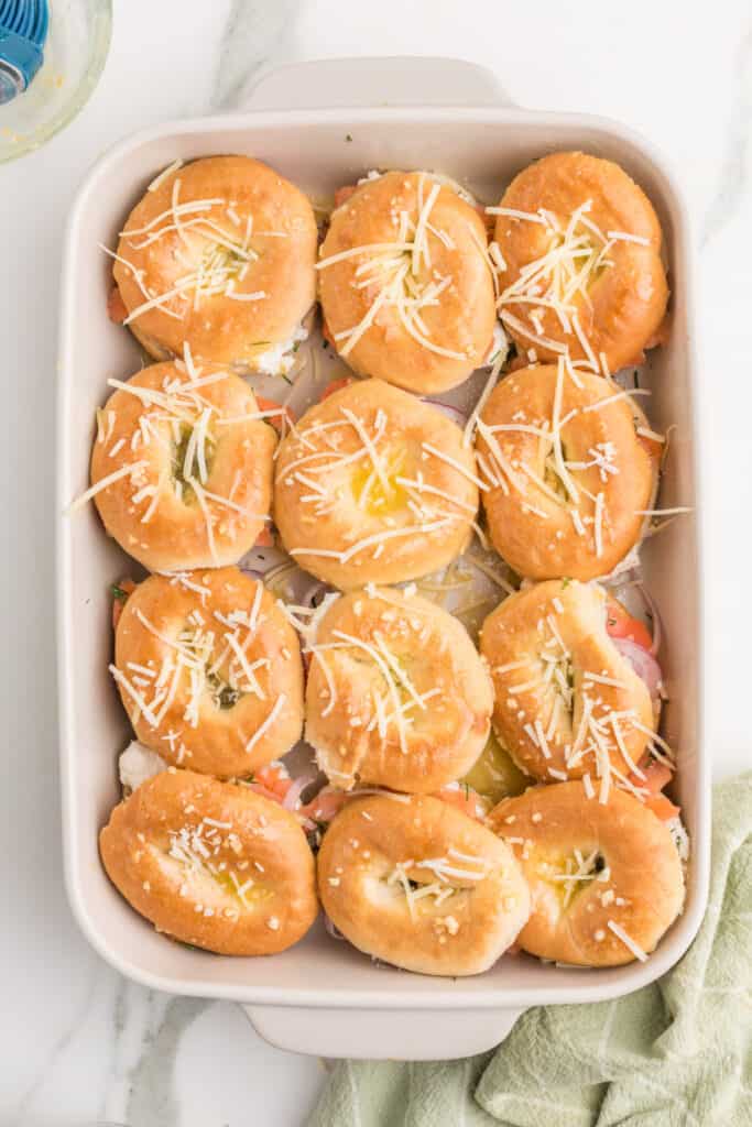 Parmesan cheese sprinkled over buttered mini bagel sliders before baking