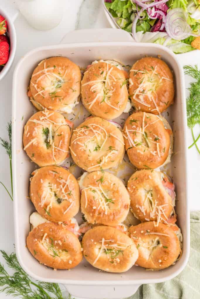 Freshly baked Bagels & Lox Sliders topped with Parmesan and fresh dill in a baking dish