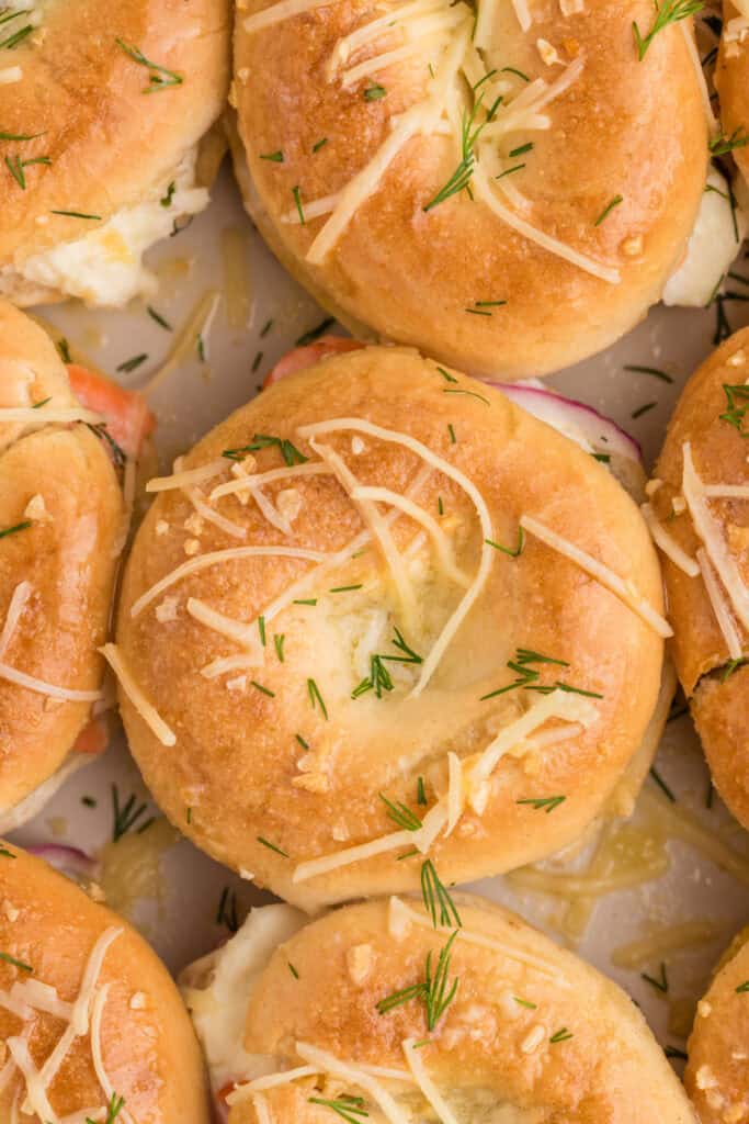 Close-up of golden baked mini bagel sliders topped with Parmesan cheese and fresh dill