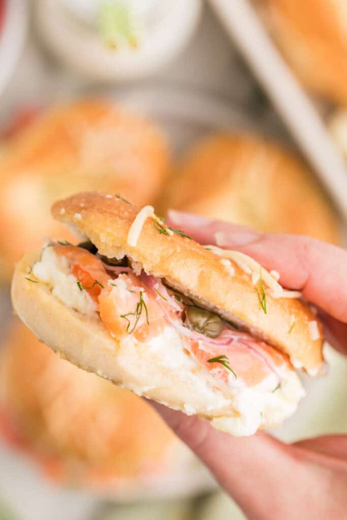 Hand holding a Baked Bagels & Lox Slider filled with smoked salmon, cream cheese, red onion, capers, and dill