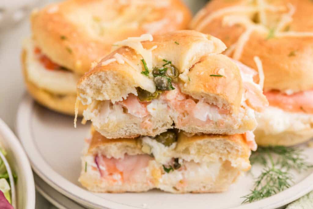 Halved Baked Bagels & Lox Sliders stacked on a plate showing the smoked salmon and cream cheese filling