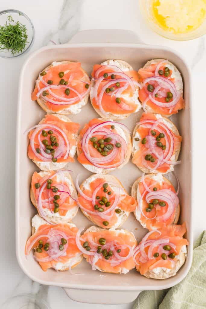 Capers scattered over smoked salmon and red onion while assembling bagel and lox sliders