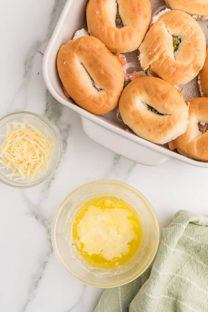 Melted butter in a bowl beside assembled Baked Bagels & Lox Sliders