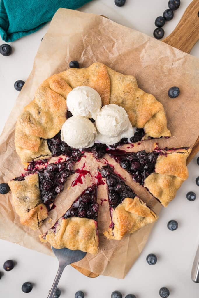 Sliced Blueberry Galette topped with scoops of vanilla ice cream and surrounded by fresh blueberries