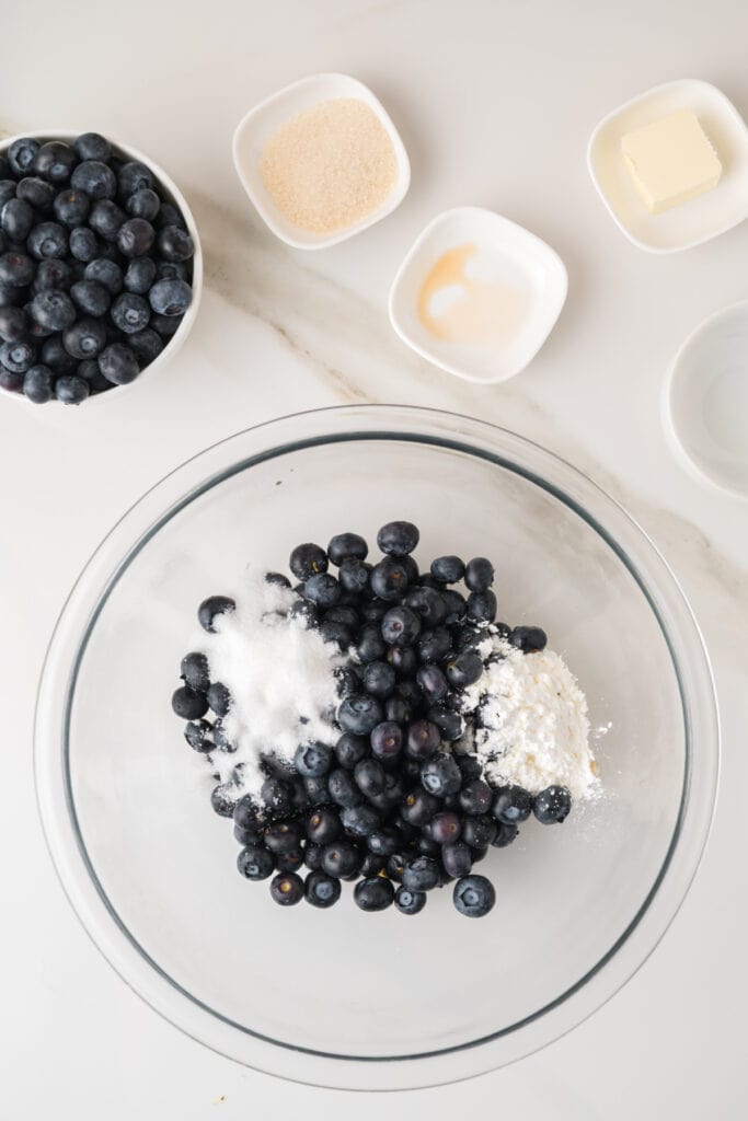Fresh blueberries with granulated sugar and cornstarch in a glass mixing bowl