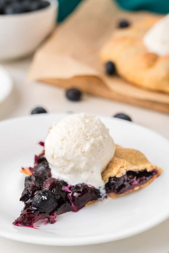 Blueberry Galette served with vanilla ice cream on a white plate with fresh blueberries in the background
