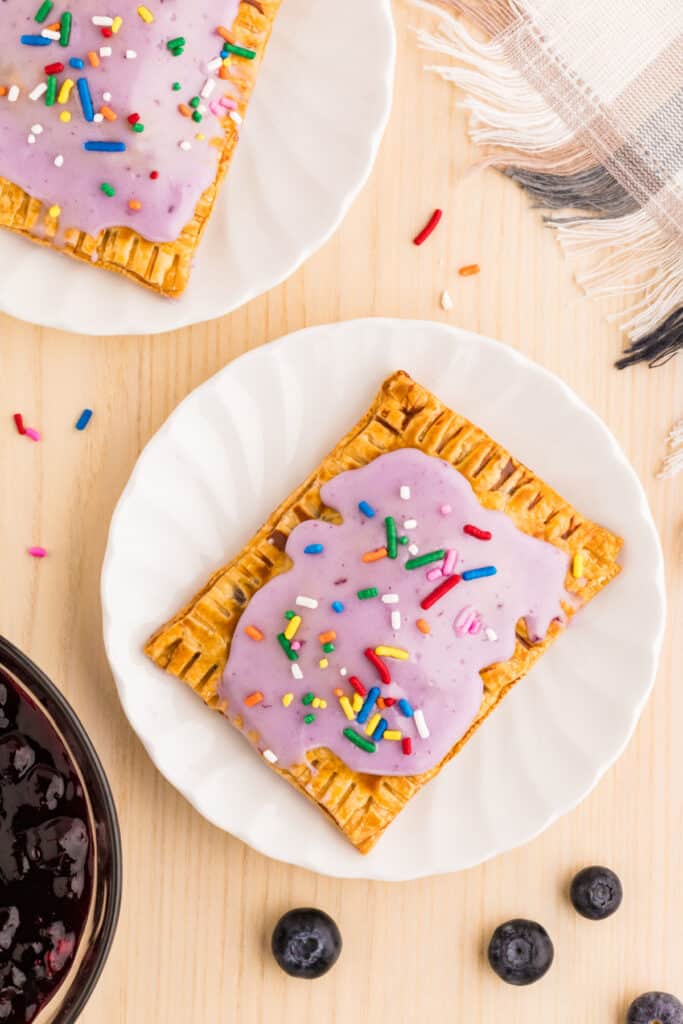Homemade Blueberry Pop-Tarts with flaky golden crust, blueberry glaze, and colorful sprinkles on white plate