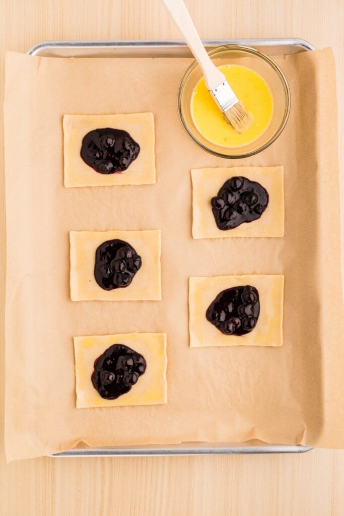 Pie crust rectangles topped with homemade blueberry filling before assembling the pastries