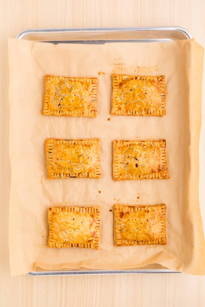 Freshly baked blueberry pastries with golden pie crust on a parchment-lined baking sheet