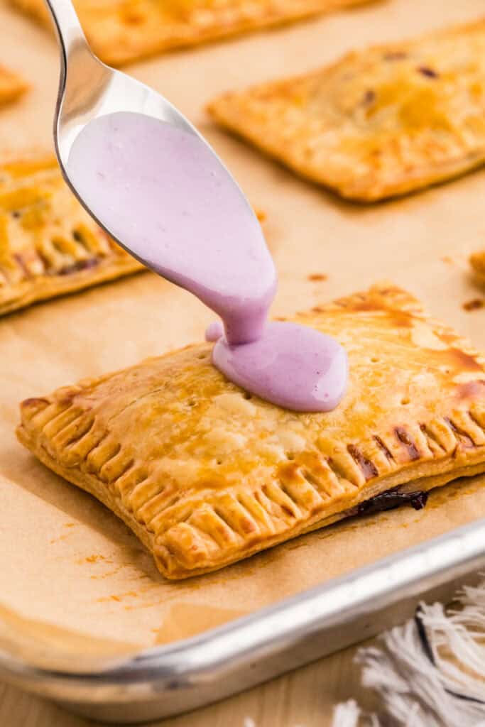 Spoon drizzling purple blueberry glaze over a freshly baked homemade Pop-Tart