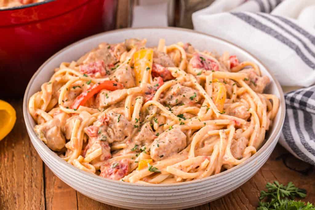 Close-up bowl of creamy chicken pasta with bell peppers, tomatoes, and fresh parsley