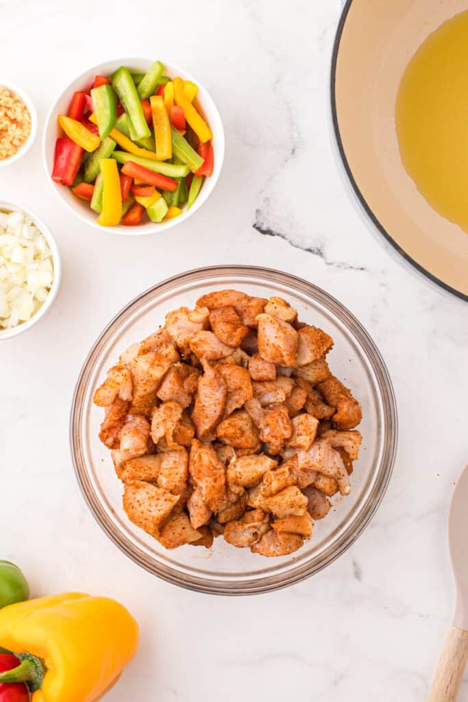 Chicken breast pieces tossed with Old Bay seasoning in a glass mixing bowl