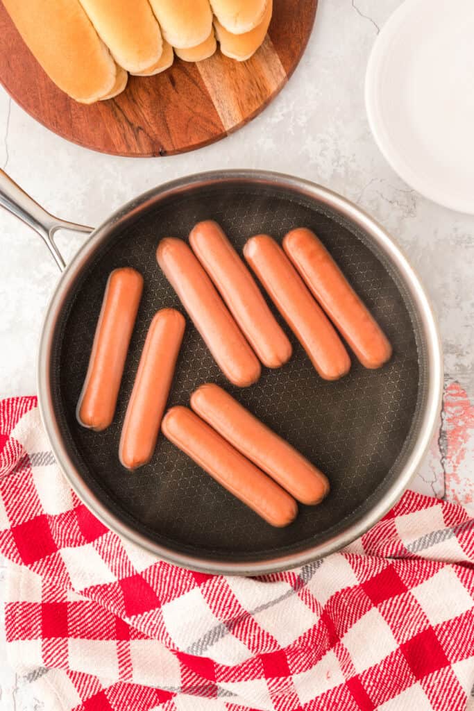 Hot dogs simmering in water in a skillet before browning for Carolina Dogs.