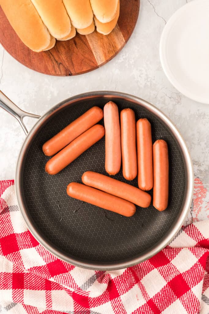 Hot dogs beginning to plump in a skillet while cooking for Carolina Dogs.