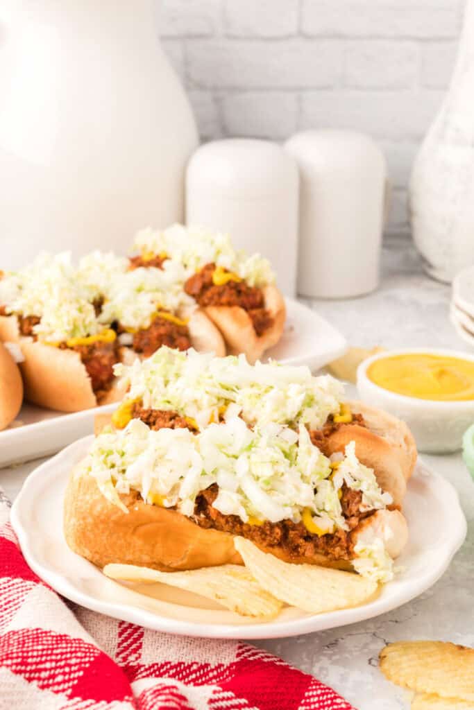 Plate with two Carolina Dogs topped with homemade hot dog chili, creamy slaw, and chopped onions, served with potato chips.