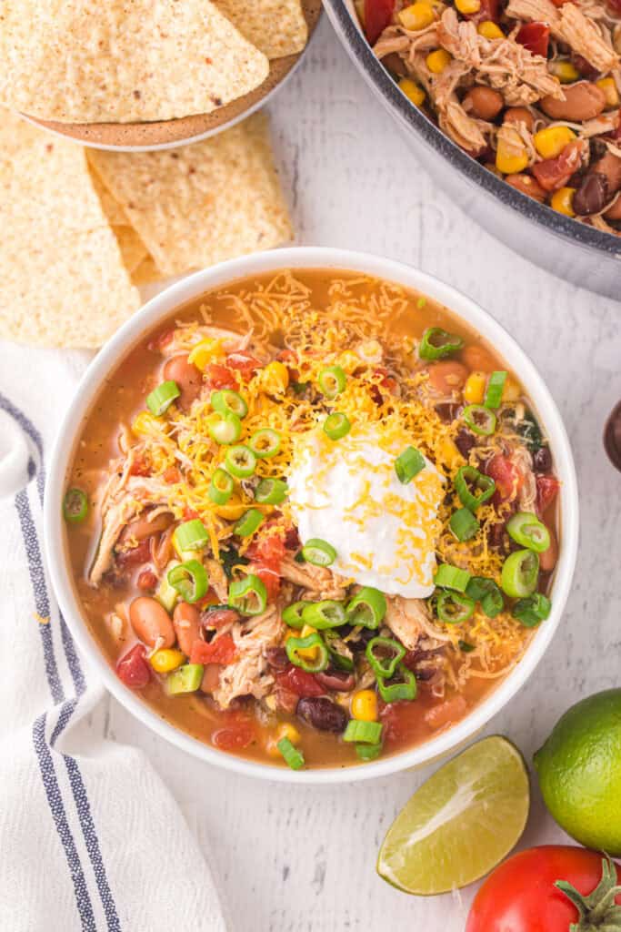 Bowl of Chicken Taco Soup topped with shredded cheddar cheese, sour cream, and chopped green onions.