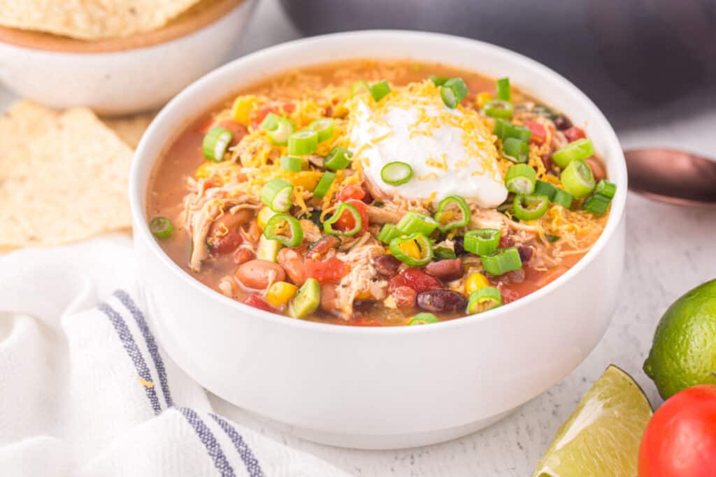 Chicken Taco Soup served in a white bowl with cheese, sour cream, green onions, tortilla chips, and fresh lime.