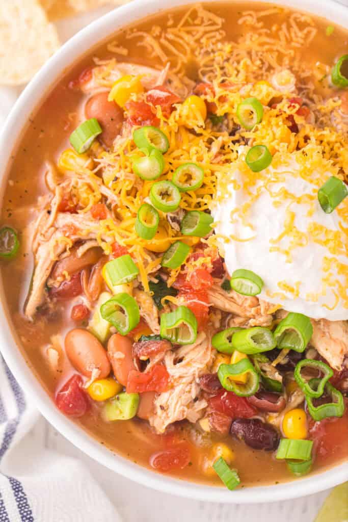 Close-up of Chicken Taco Soup topped with cheddar cheese, sour cream, and sliced green onions.