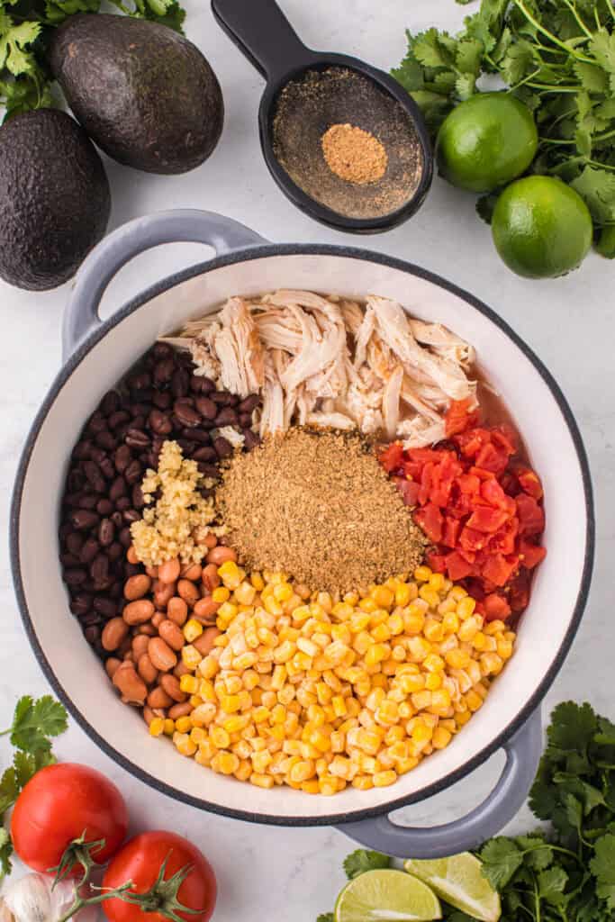 Shredded chicken, black beans, pinto beans, corn, tomatoes, garlic, and taco seasoning added to a pot for Chicken Taco Soup.