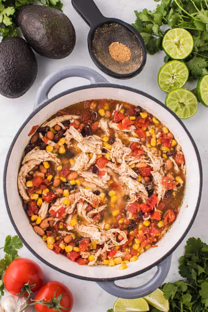 Chicken Taco Soup simmering in a large pot with shredded chicken, black and pinto beans, corn, and tomatoes.