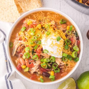 Bowl of easy Chicken Taco Soup topped with shredded cheddar cheese, sour cream, and green onions.