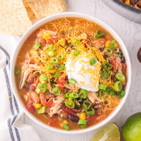 Bowl of easy Chicken Taco Soup topped with shredded cheddar cheese, sour cream, and green onions.