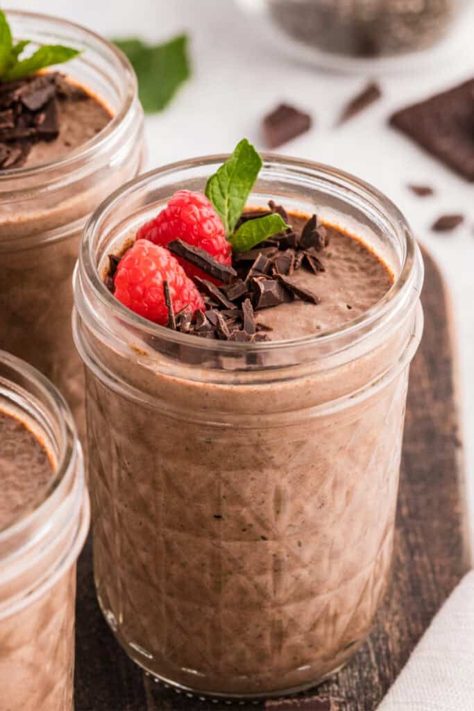 Creamy chocolate chia pudding jars topped with raspberries, chopped dark chocolate, and fresh mint
