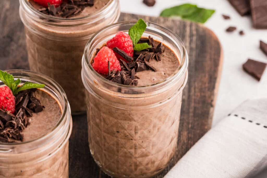 Three jars of Chocolate Chia Pudding topped with raspberries, dark chocolate, and mint
