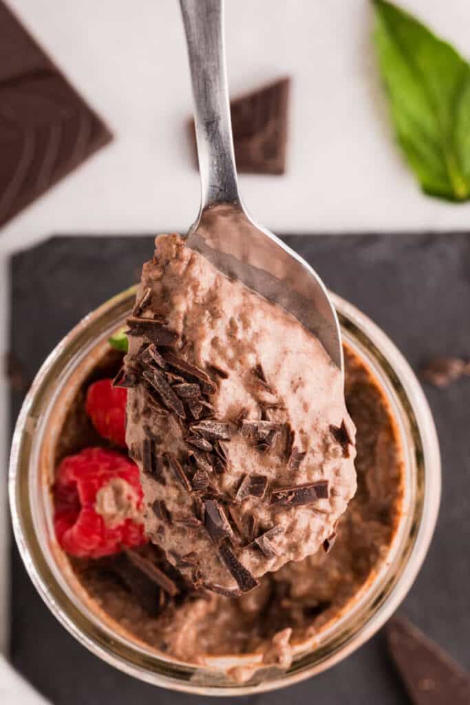 Spoonful of thick Chocolate Chia Pudding topped with dark chocolate over a glass jar with raspberries