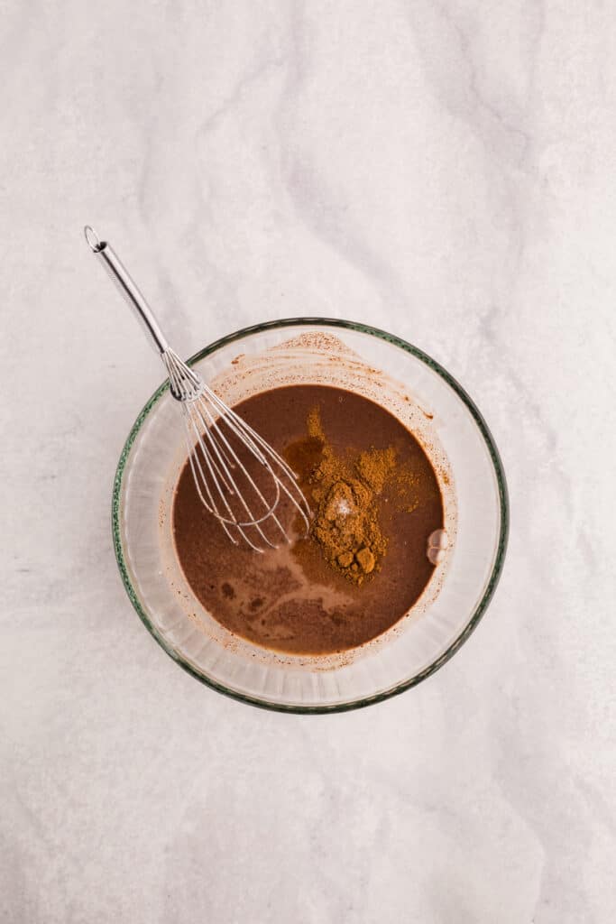Cinnamon added to melted chocolate mixture in a glass bowl with a whisk