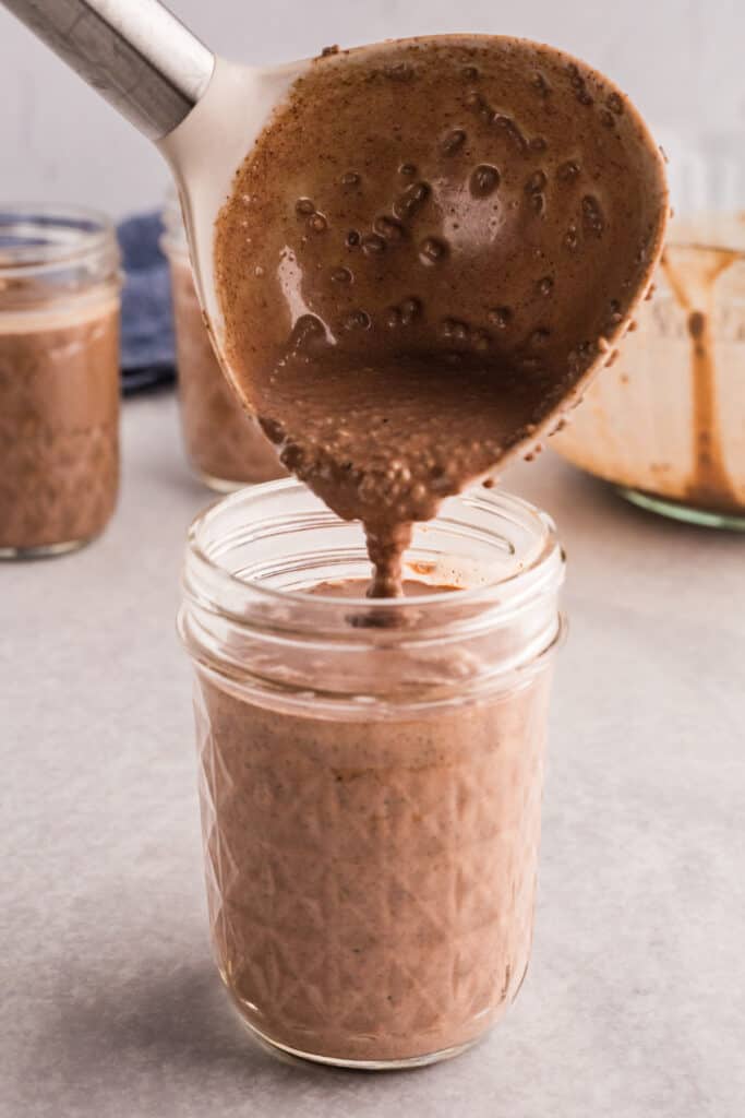 Chocolate chia pudding mixture being spooned into individual glass jars