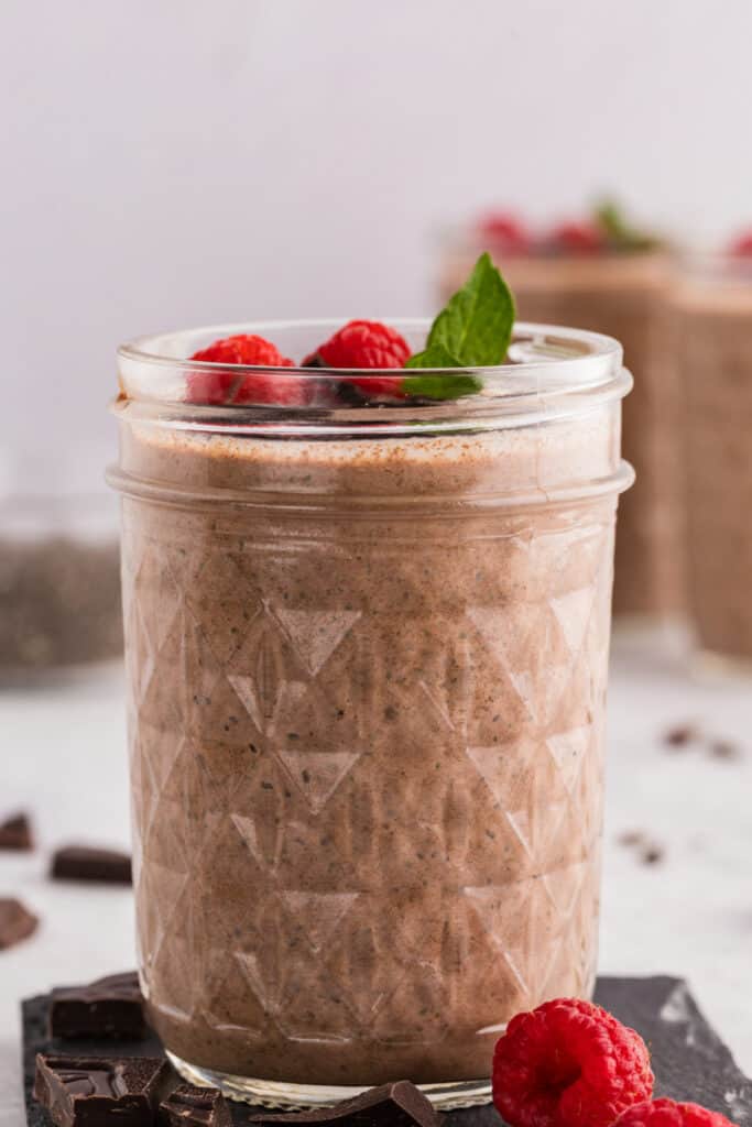 Chocolate Chia Pudding in a glass jar topped with fresh raspberries, mint, and dark chocolate