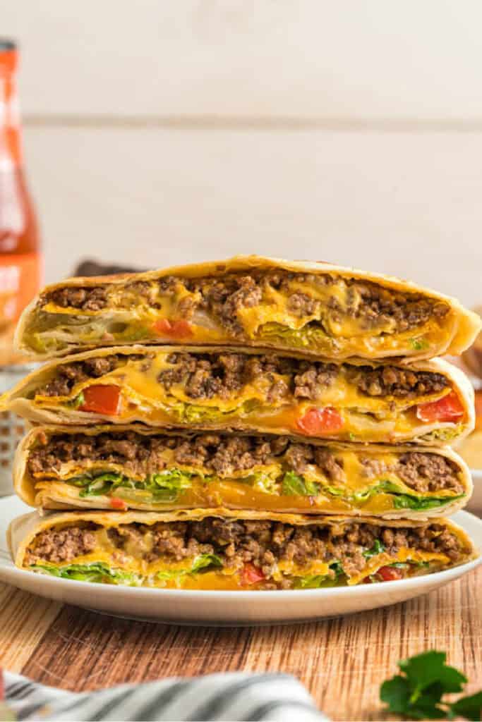 Stack of cut Crunchwrap Supremes showing layers of beef, cheese, lettuce, and tomatoes