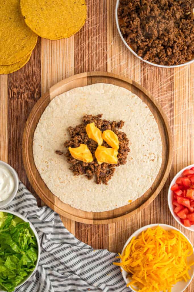 Nacho cheese sauce added over seasoned beef on a flour tortilla