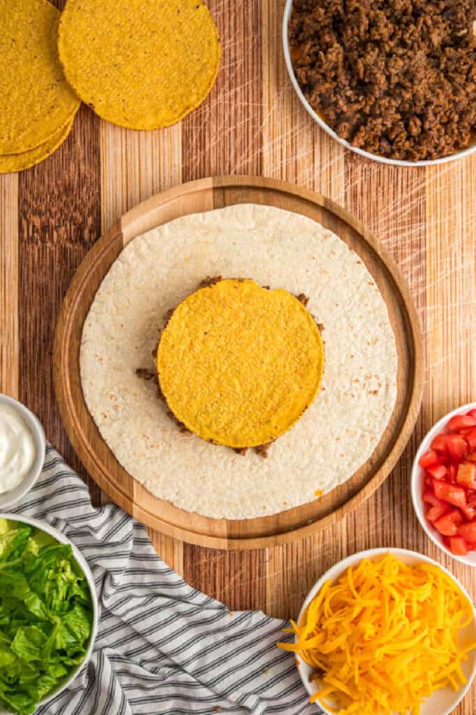 Tostada placed over beef and nacho cheese while assembling a Crunchwrap