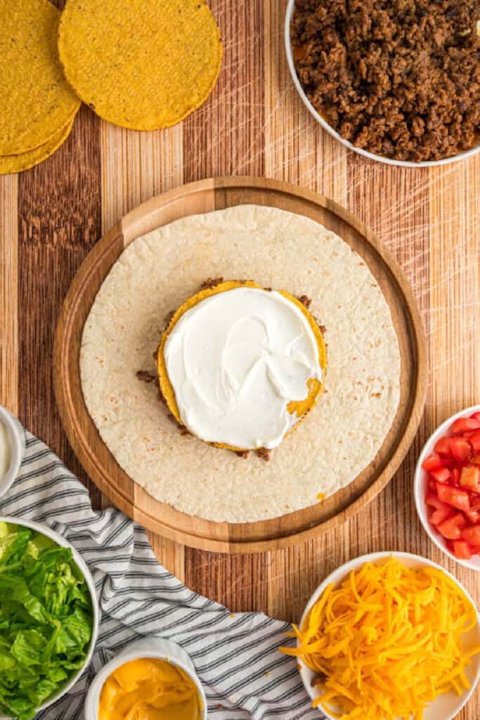 Sour cream spread over the tostada for a homemade Crunchwrap