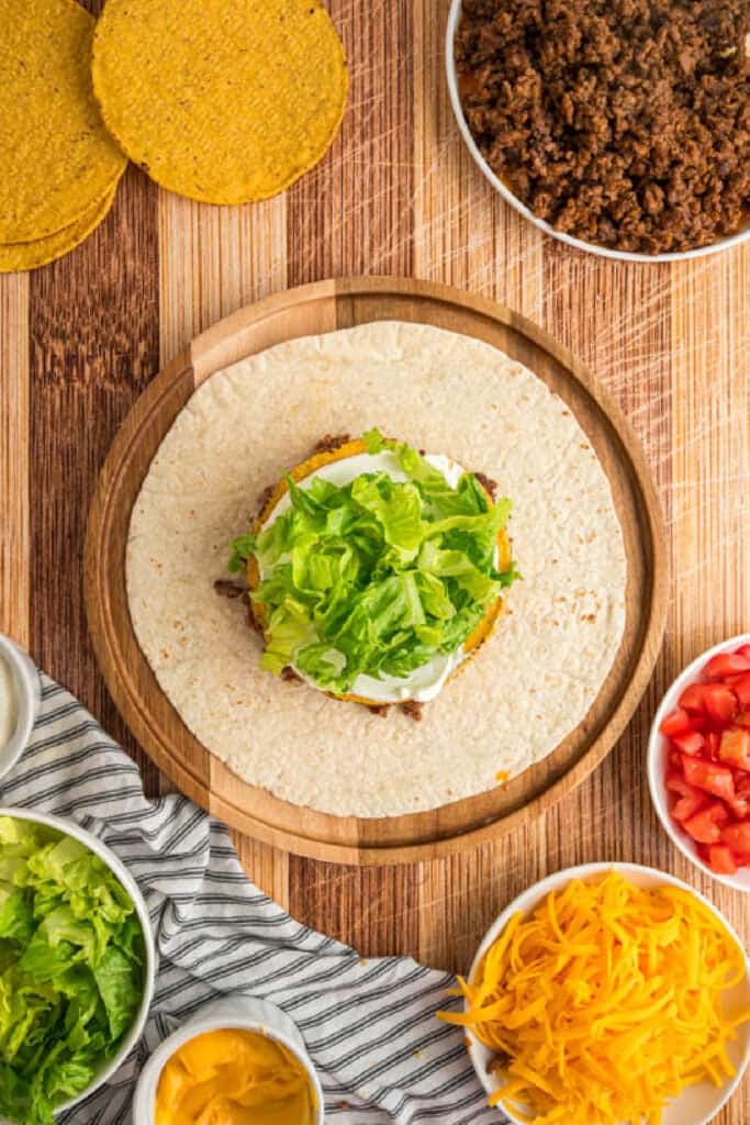 Shredded lettuce layered over sour cream while assembling a Crunchwrap