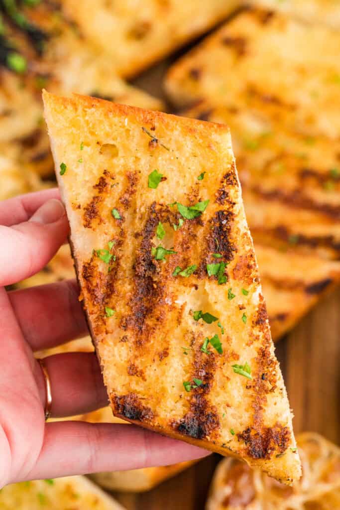 Hand holding a slice of Grilled Garlic Bread showing the crispy grilled surface and buttery interior.