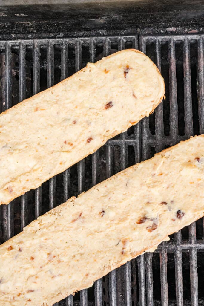 Buttered French bread placed on grill grates before cooking for Grilled Garlic Bread.