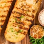 Square overhead photo of Grilled Garlic Bread served with roasted garlic, Parmesan cheese, and fresh parsley.