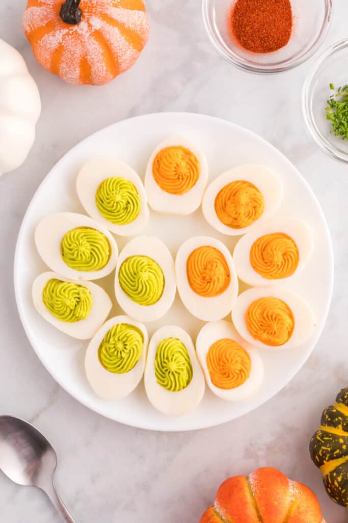 Halloween deviled eggs filled with bright orange and neon green creamy yolk filling on a white serving plate.