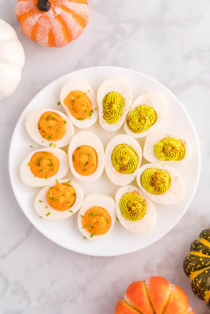 Finished Halloween deviled eggs with orange filling and chives alongside green filling sprinkled with paprika.