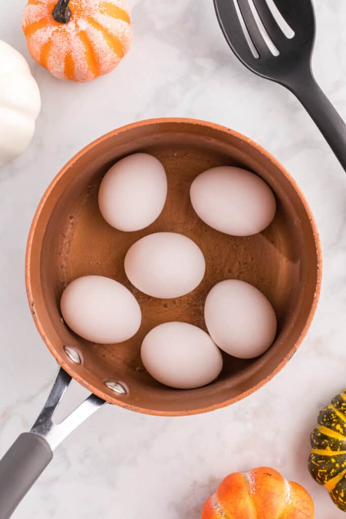 Six eggs cooking in a saucepan for an easy Halloween deviled eggs recipe.