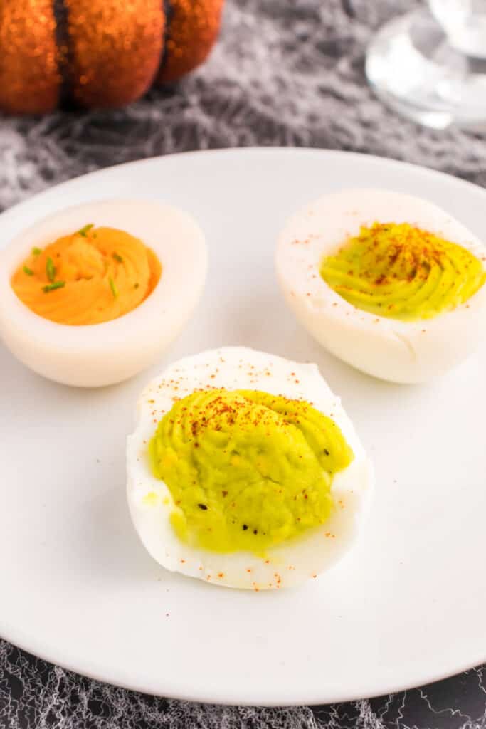 Close-up of orange and neon green Halloween deviled eggs garnished with chopped chives and paprika.