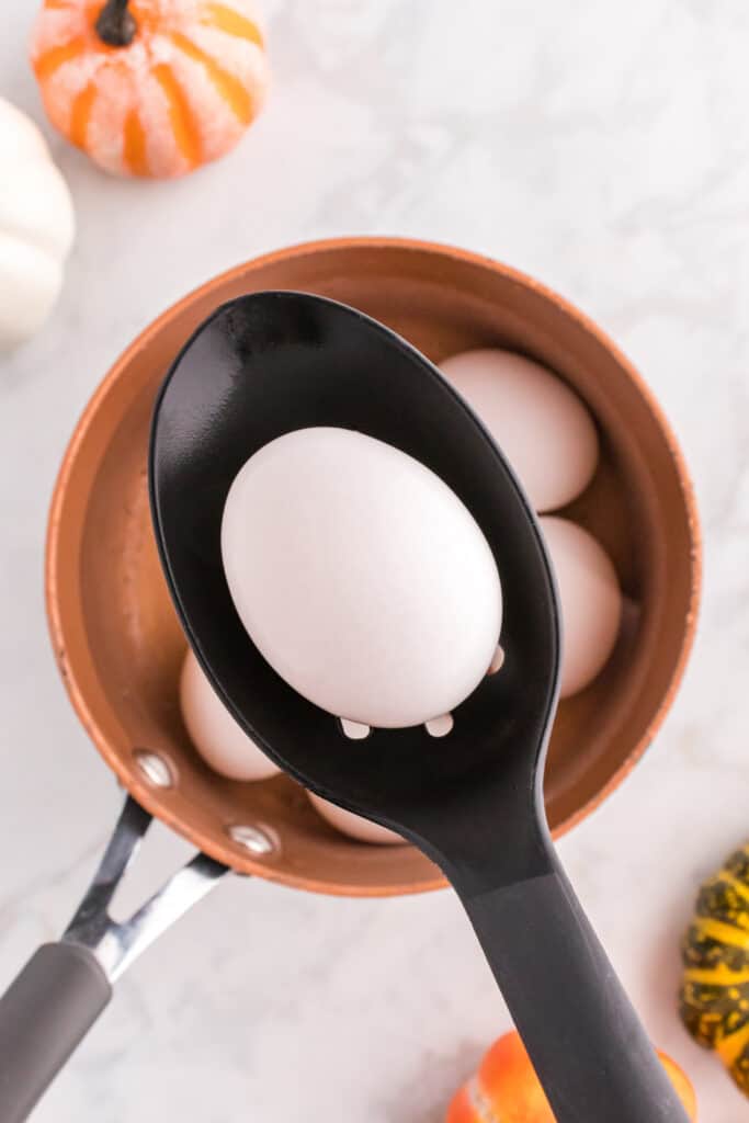 Hard-boiled egg being removed from a saucepan with a slotted spoon.